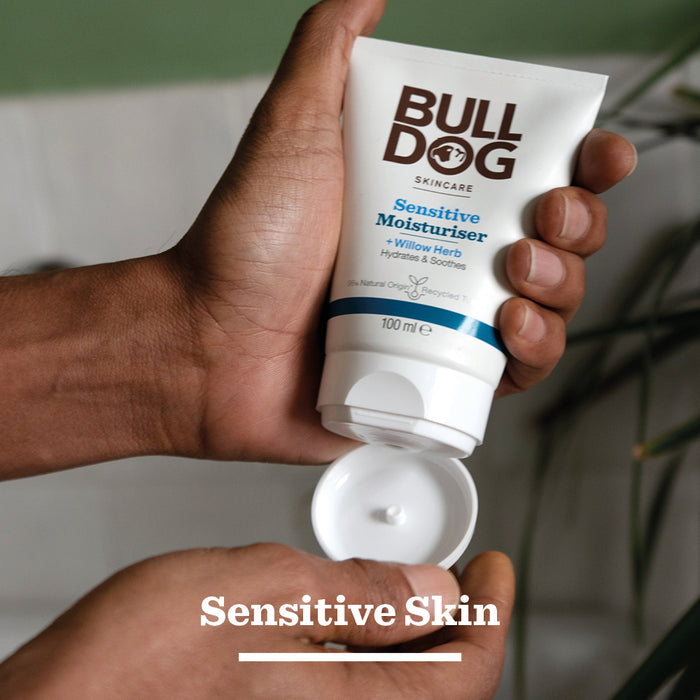 A person holds an open tube of Sensitive Moisturiser, squeezing some onto their hand. The label features willow herb, hydration, and natural origin ingredients. “Sensitive Skin” appears at the bottom.