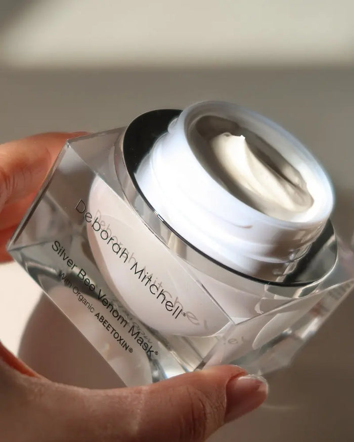 Deborah Mitchell silver bee venom mask held by a hand against a neutral background