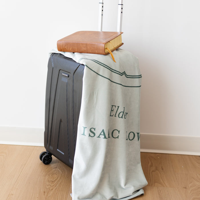 LDS missionary blanket featuring The Gathering design, displayed over luggage with scriptures, symbolizing missionary preparation and service.