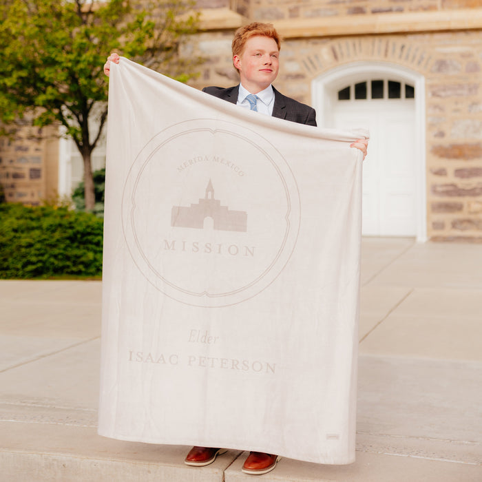Young man holding The Lord's House LDS temple blanket outside a church building, featuring temple artwork and faith-centered design.