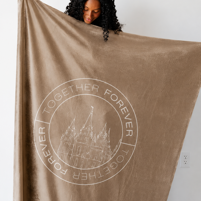 Person holding a cocoa brown LDS blanket featuring a temple design and the words "Together Forever," soft faith-inspired throw blanket celebrating eternal families and lasting connections.