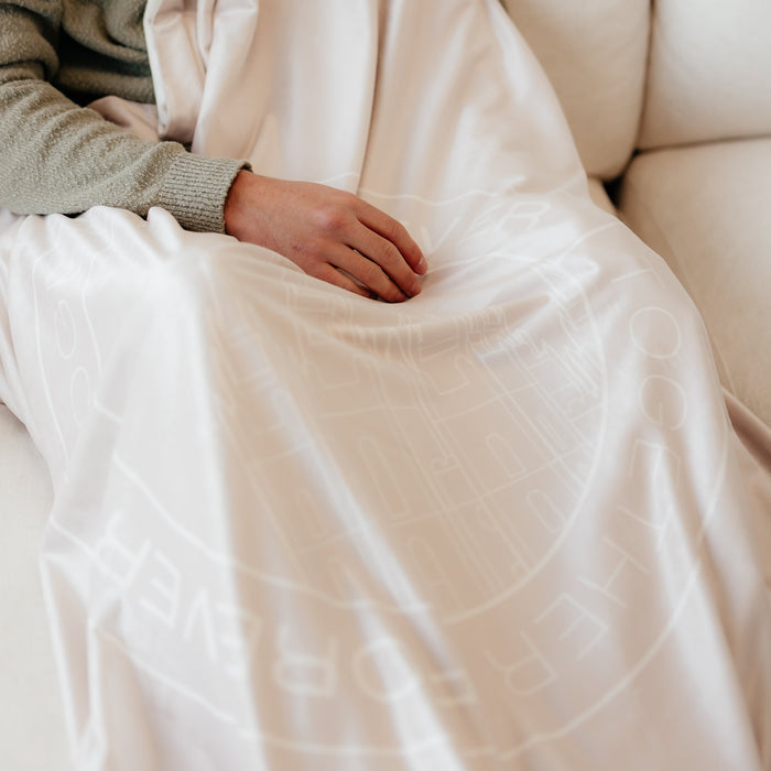 Person wrapped in a soft oat cream LDS blanket featuring a subtle temple design and the words "Together Forever," cozy faith-inspired throw blanket celebrating eternal families and lasting connections.