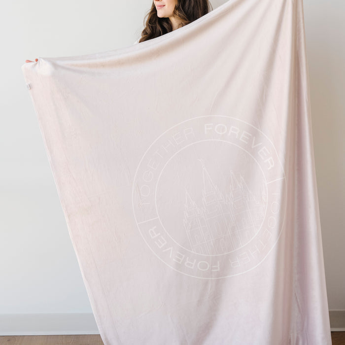 Person holding a soft oat cream LDS blanket featuring a temple design and the words "Together Forever," faith-inspired throw blanket celebrating eternal families and lasting connections.