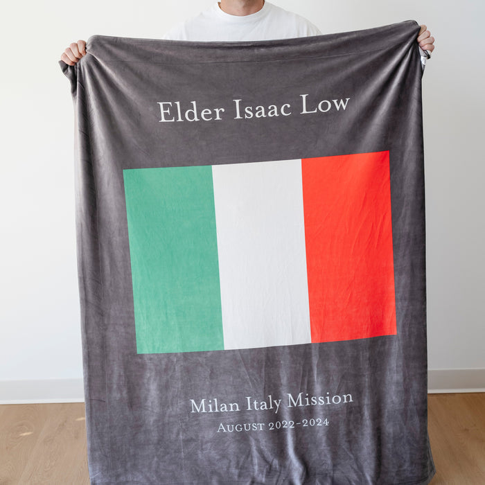 Person holding a personalized missionary blanket featuring the Milan Italy Mission flag, missionary name, and custom mission dates.
