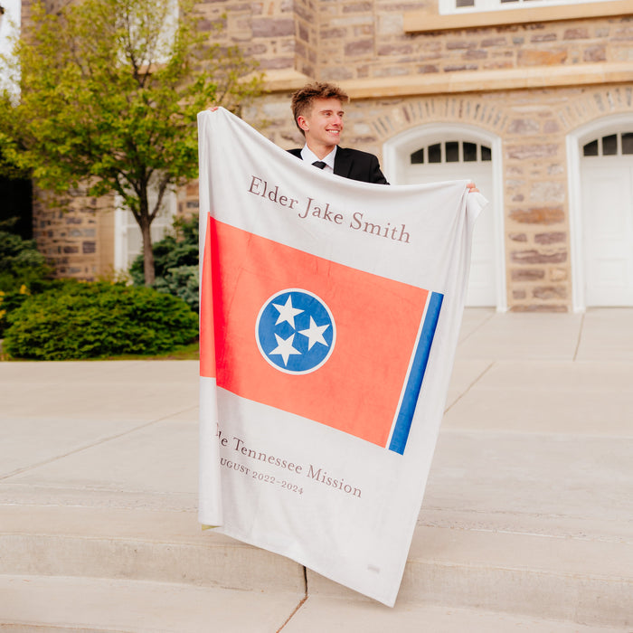 Missionary holding a personalized mission flag blanket featuring a custom name, mission flag, and service dates, meaningful LDS missionary gift for mission farewells and homecomings.