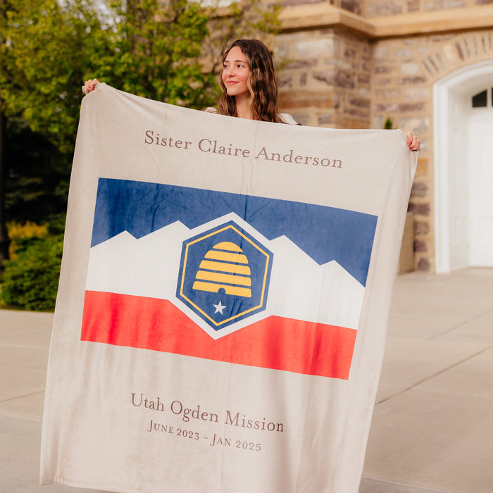 Personalized missionary blanket featuring the Utah Ogden Mission name, mission dates, and mission flag design, displayed outdoors.