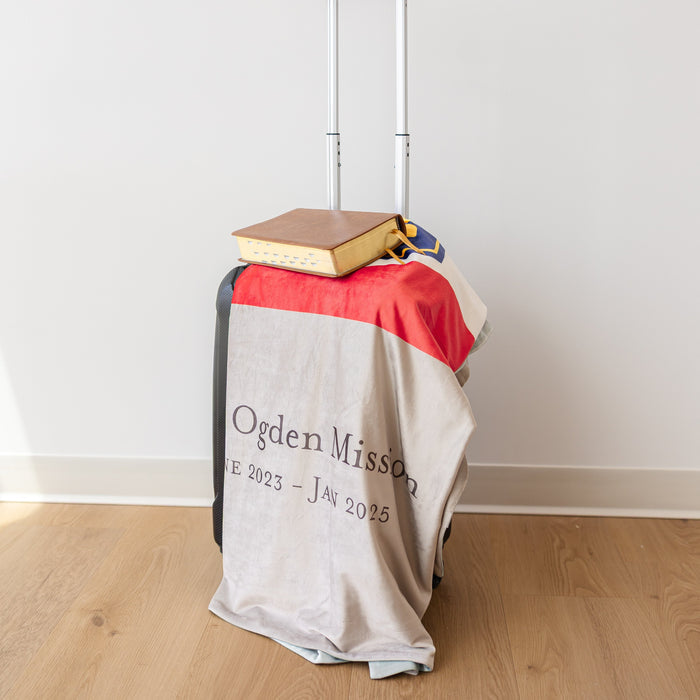 Personalized missionary blanket featuring the Utah Ogden Mission name and mission dates, displayed with scriptures in a home setting.