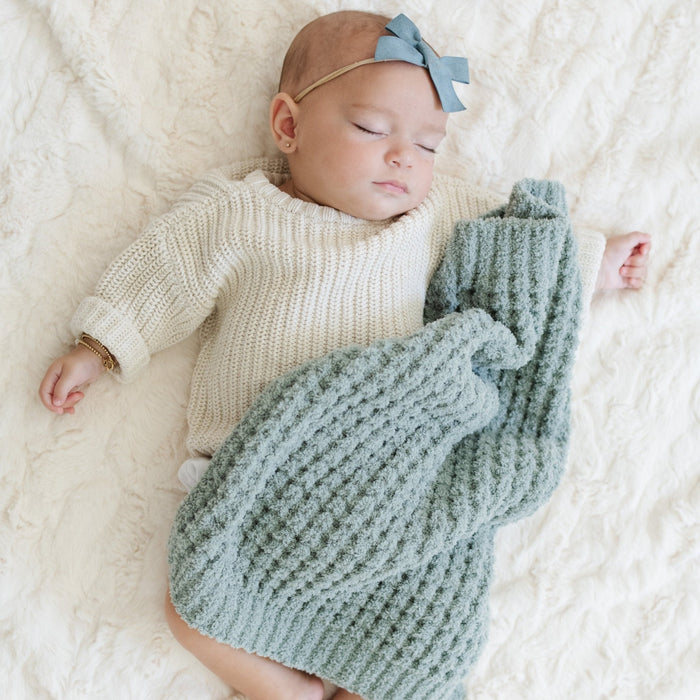 Sleeping baby girl snuggled up with blue waffle knit blanket.