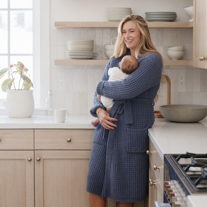 Mother holding baby at home while wearing blue waffle knit robe.