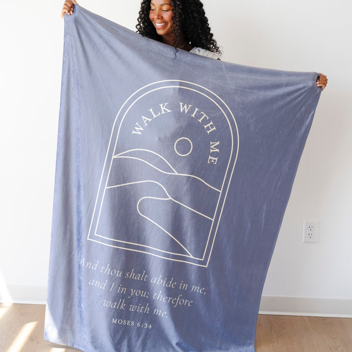 Woman holding a haze blue LDS youth theme blanket featuring the words "Walk With Me" and a scripture-inspired landscape design, faith-centered throw blanket inspired by the 2026 LDS Youth Theme.