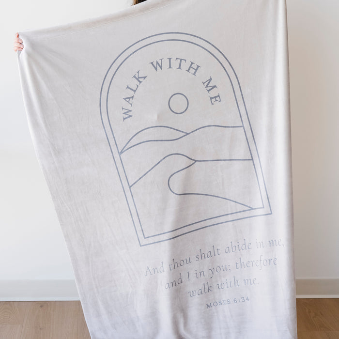 Person holding a desert cream LDS youth theme blanket featuring the words "Walk With Me" and a scripture-inspired landscape design, faith-centered throw blanket inspired by the 2026 LDS Youth Theme.